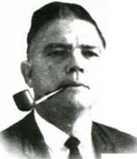 Portrait of Taylor, wearing a suit and tie and holding a pipe in his mouth