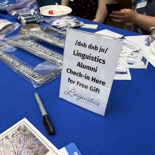 Free swag for WWU LING alumni with a sign that says "Linguistics Alumni Check-in Here for Free Gift. Linguistics. Western Washington University."