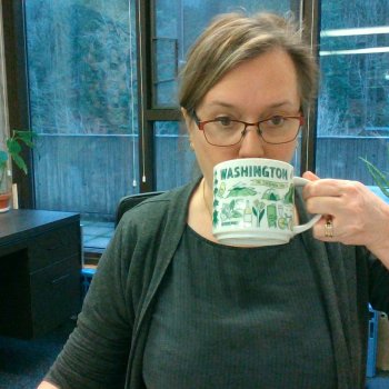 Lauren drinks from a Washington-themed coffee mug, while wearing a green cozy professional outfit