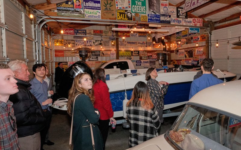 People gathered in a garage decorated with political bumper stickers