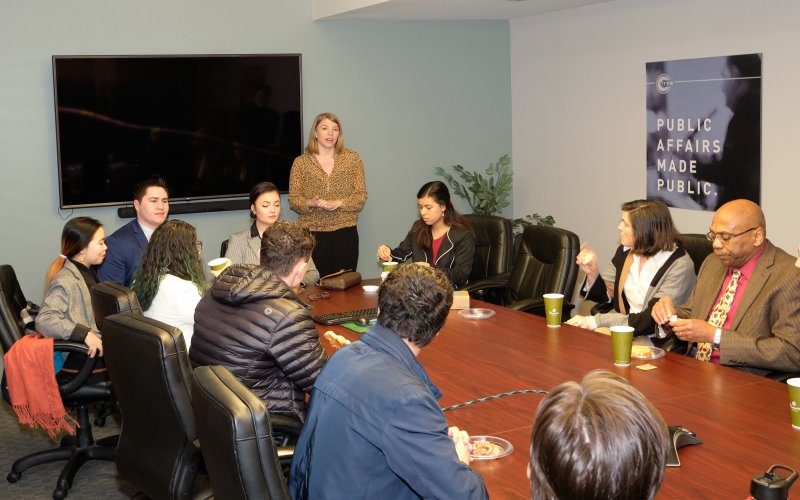 A woman addressing a group of people gathered at a conference table