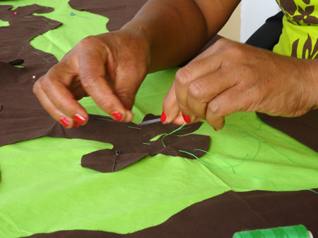 A pair of hands apply a pattern to a piece of cloth in a traditional manner