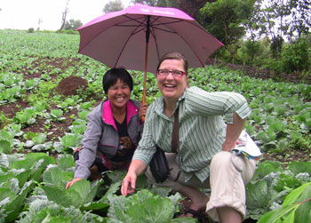 Judy Pine smiles under a pink umbrella with a friend, in a field of wide leafed plants.