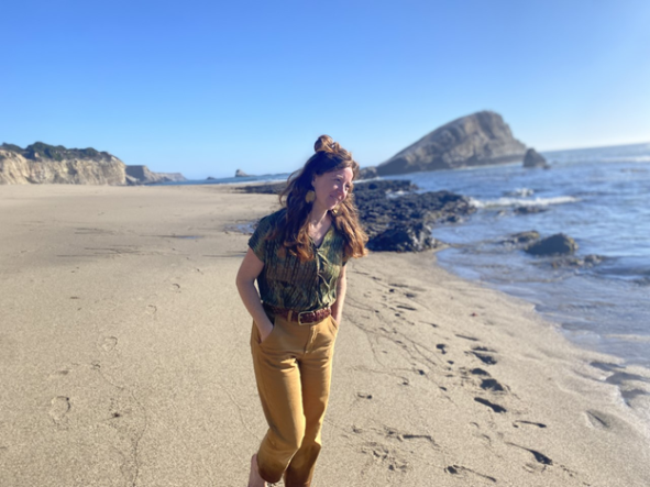 Natalie walking along the ocean on a sandy beach in CA