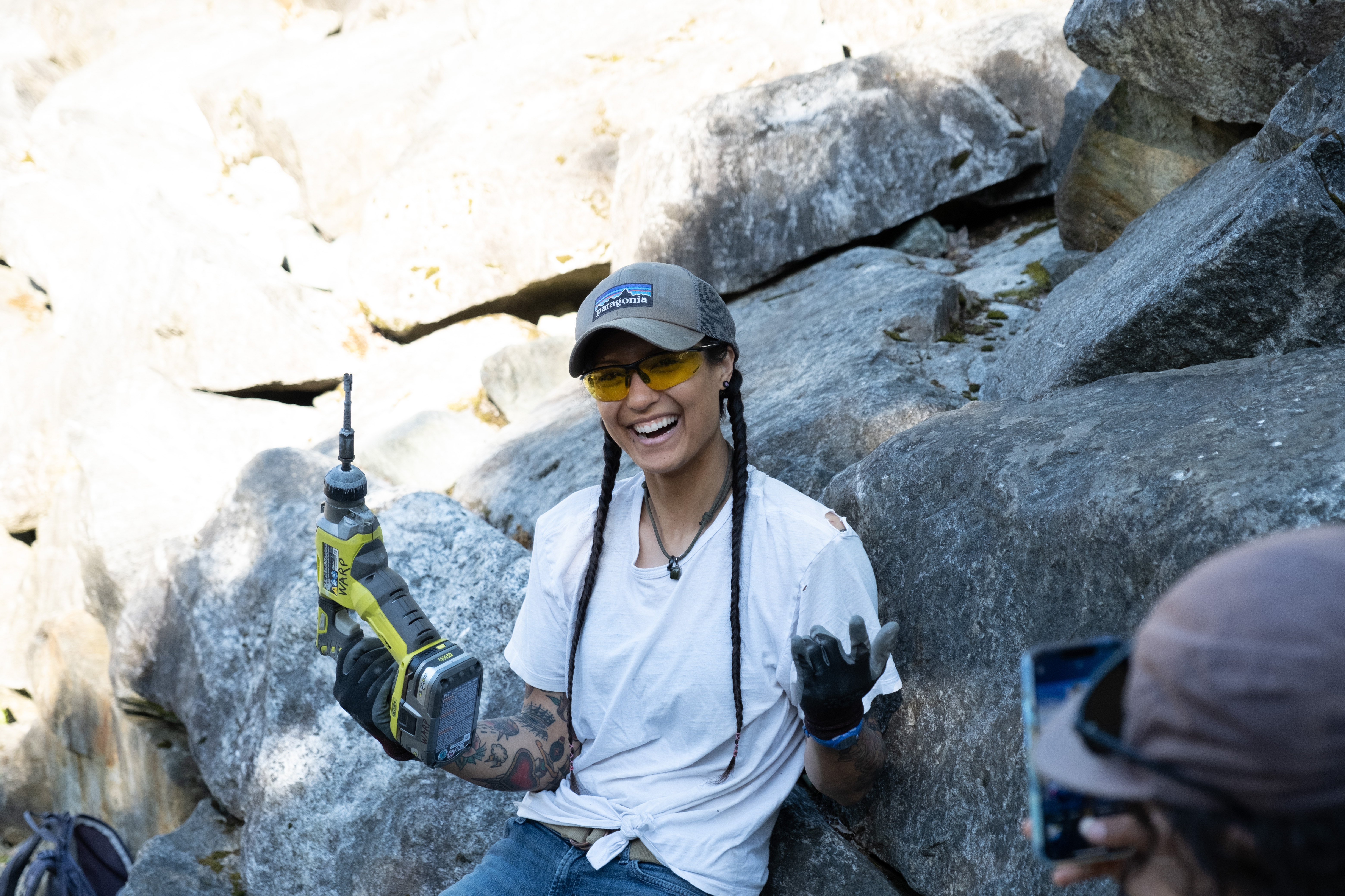Alicia sitting on a rock smiling and holding a drill