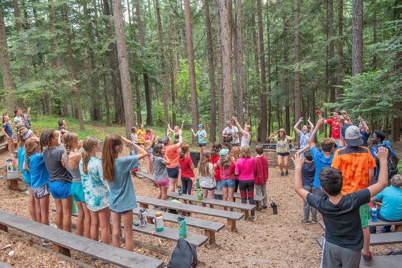 group of campers standing in forest singing with hands up