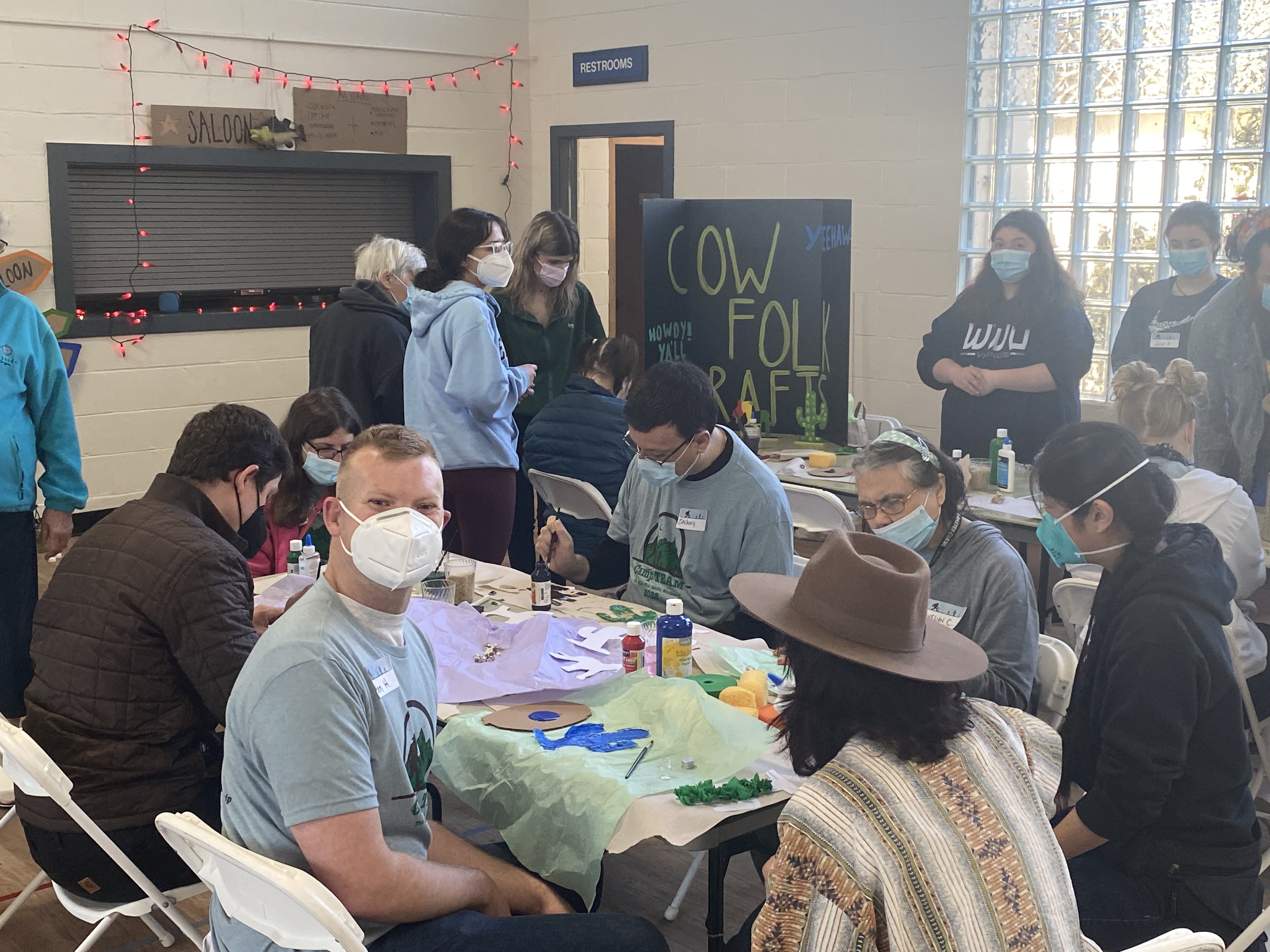 Students sitting at two tables, painting art projects