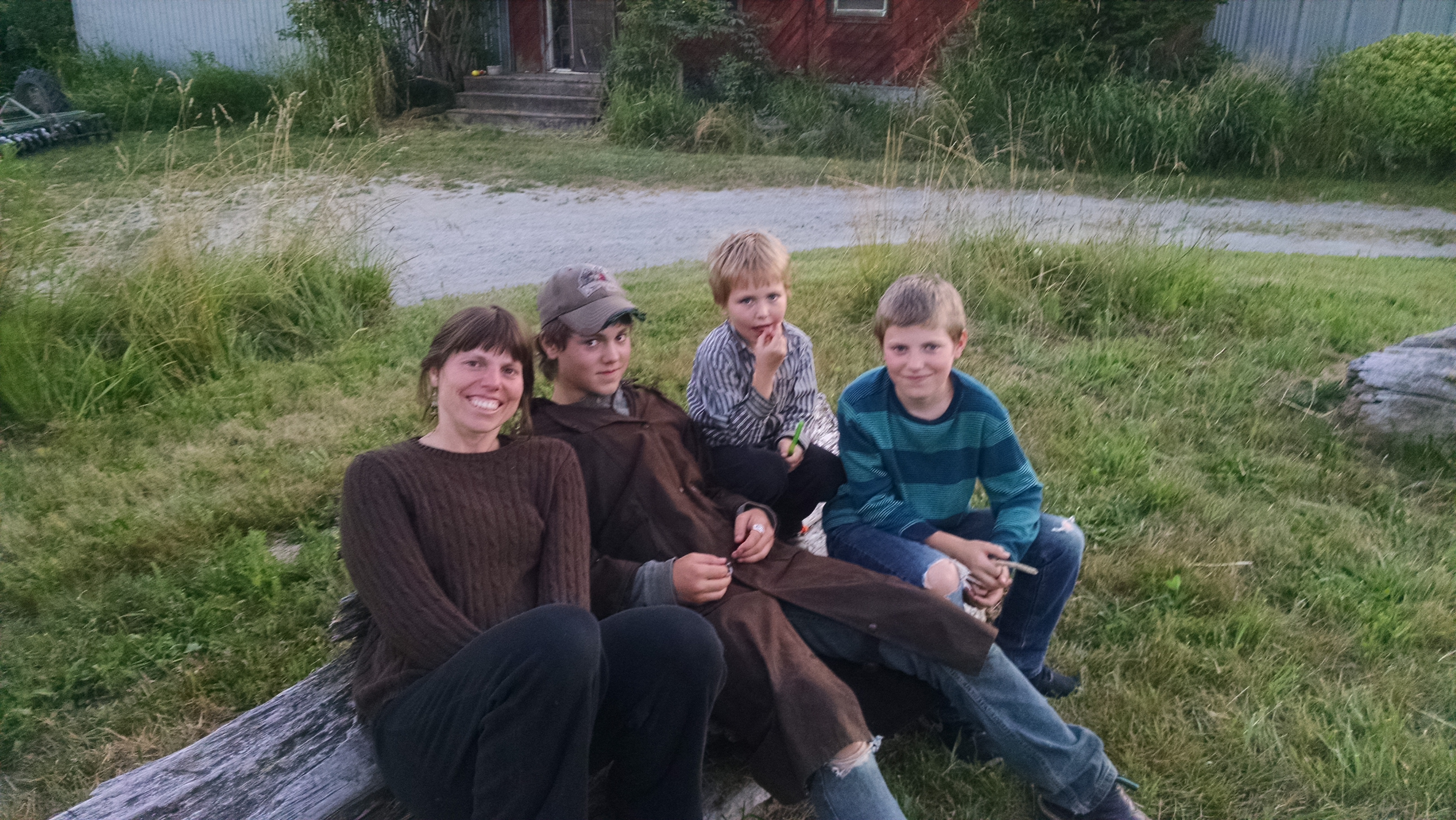 Danielle and three boys sitting on a log, smiling up at the camera