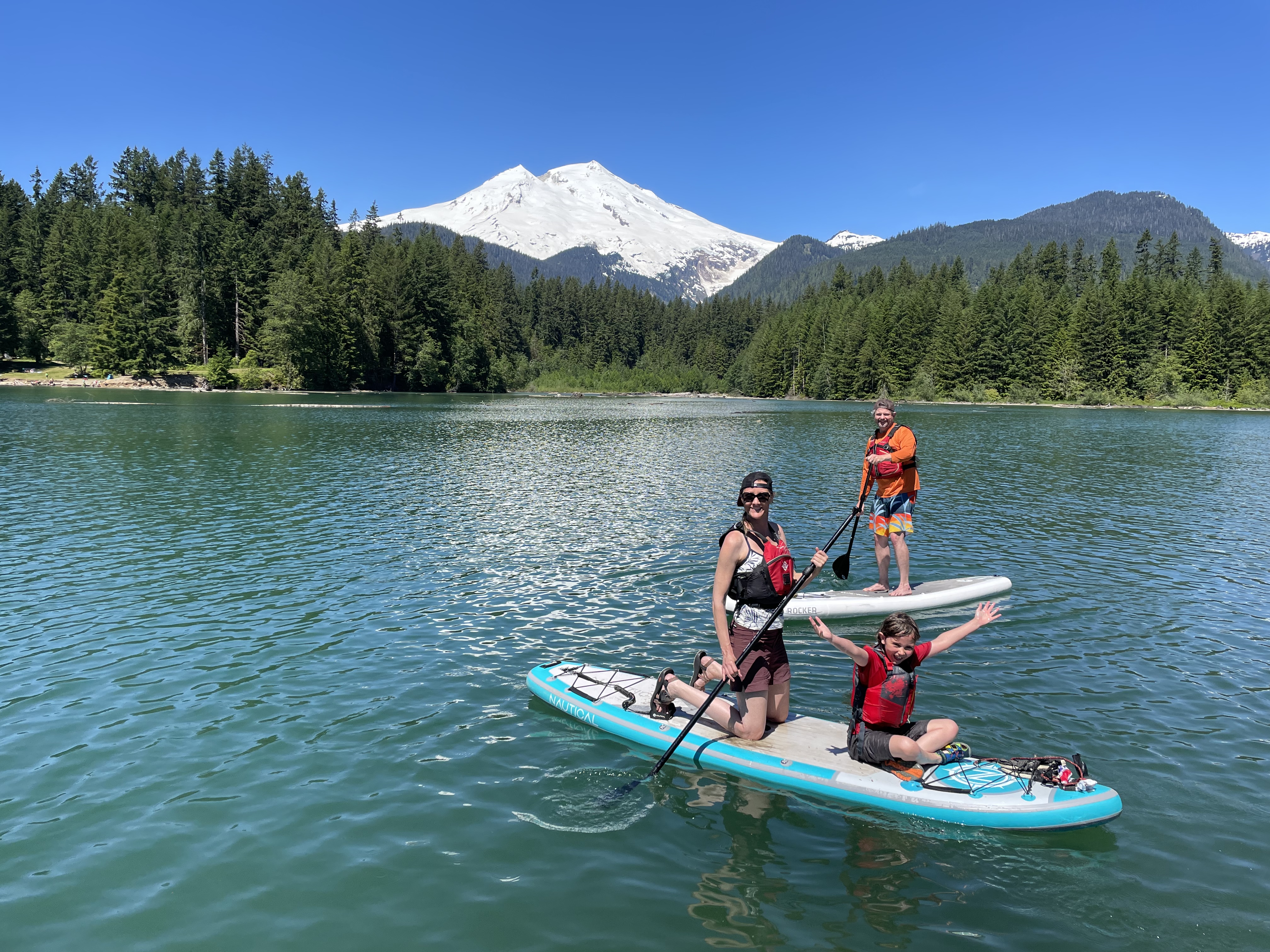 Woman and boy on paddle board and man on paddle board on a lake with a mountain and forest in the background
