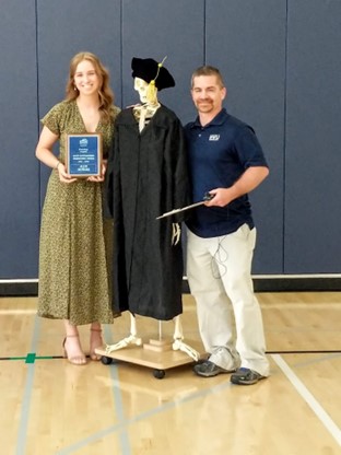 Professor, model skeleton in graduation robes and student standing together smiling