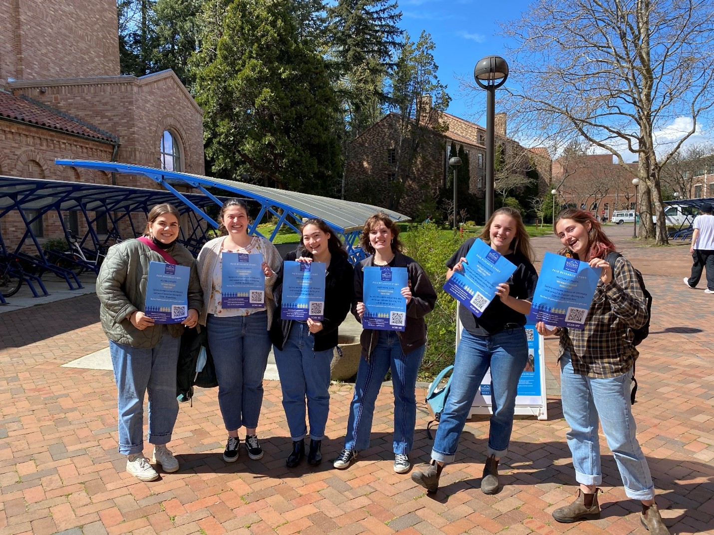 Six students holding blue posters and smiling