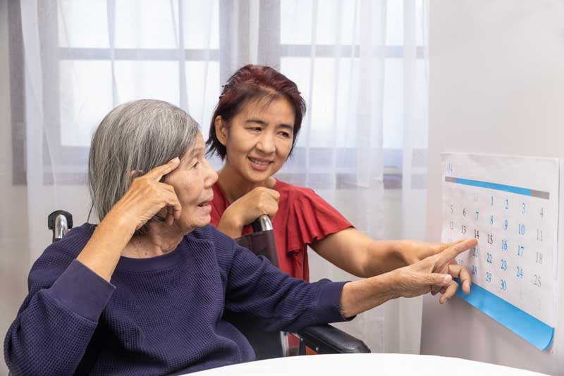 A speech pathologist clinician and a patient in a wheelchair look at a calendar
