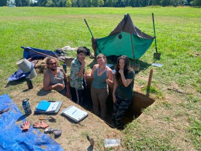 4 students/participants on an archaeological dig in an rectangular hole in the ground