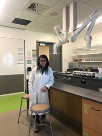 Ying in lab coat standing in a lab smiling