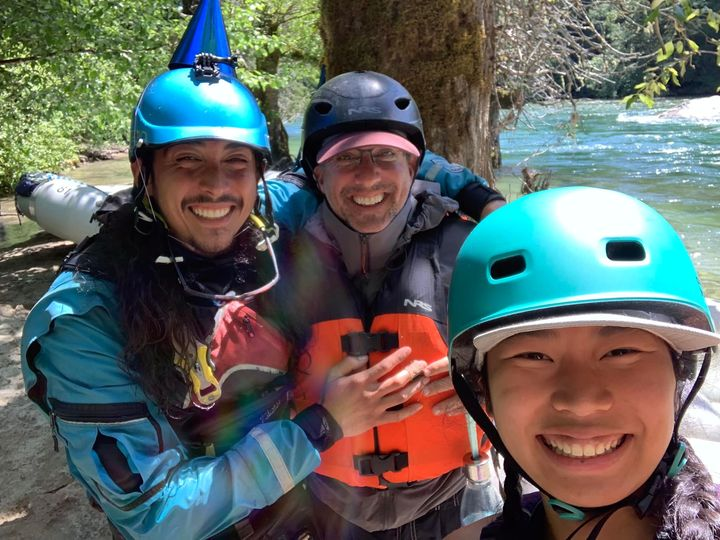Randy and two students wearing helmets smiling in front of river 