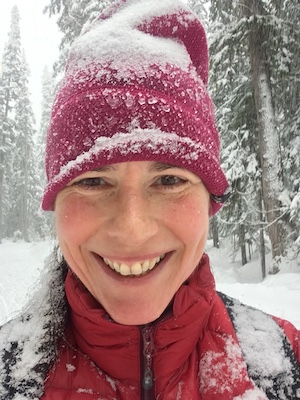 Holly Folk standing in a snowy forest with a red hat and jacket smiling