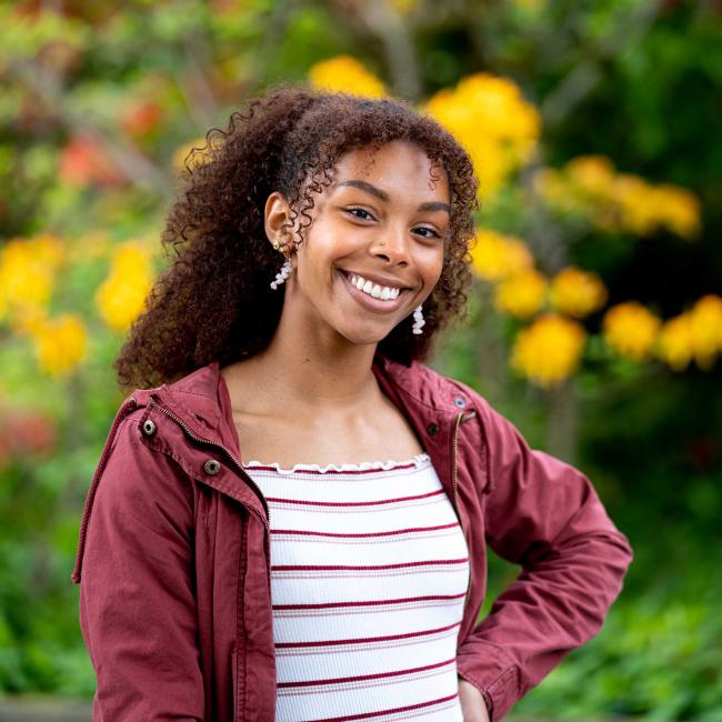 Aliyah Dawkins in a red jacket and striped shirt in front of yellow flowers