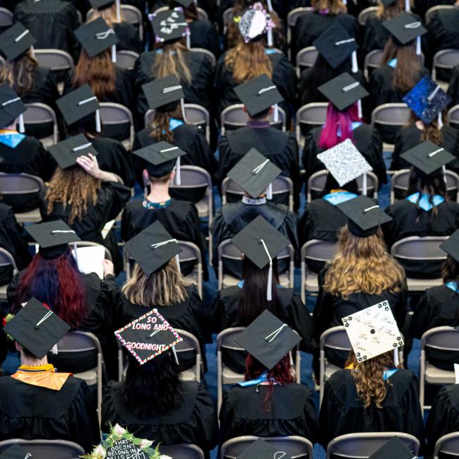 Rows of graduates sitting, grad caps in various states of decoration.