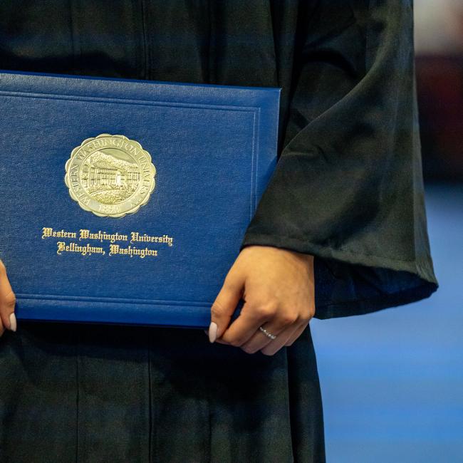 Someone holding a Western Washington University degree dressed in a graduation robe