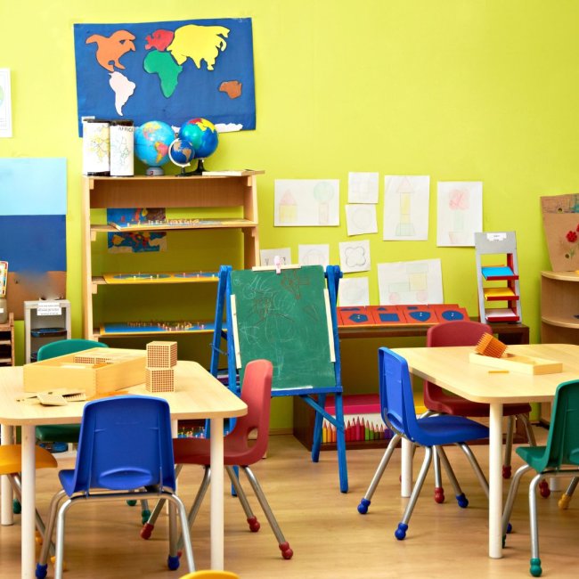 Elementary school classroom with colorful world map, children's art on the wall, and small tables and chairs.