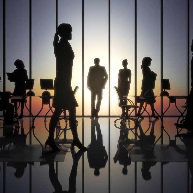 Silhouettes of 5 employees at an office with computers and a window in the background.