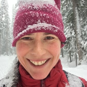 Holly Folk standing in a snowy forest with a red hat and jacket smiling