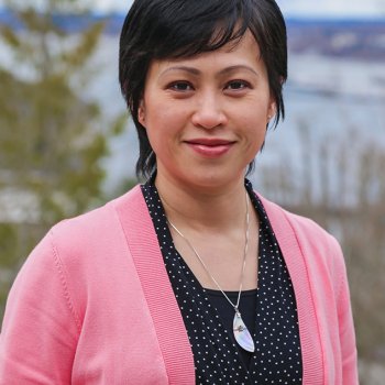 Dr. Ee Lin Lee - Chair, Professor wears a pink sweater and stands outside in front of Bellingham Bay.