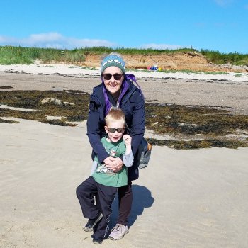 M.J. hugs a child around 7 years of age while on a beach with sand, rock, and seaweed