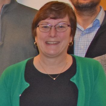 Joan Hoffman, smiling, standing inside with other professors in background