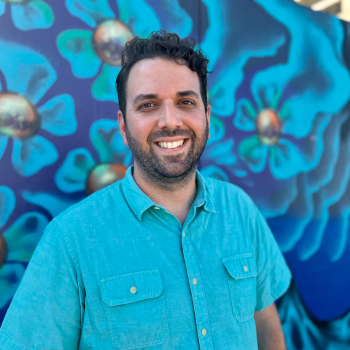 Professor Celaya smiling in front of a blue mural. 
