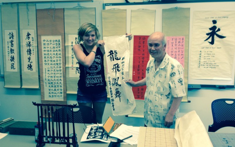 A student holding calligraphy work on cloth next to a teacher
