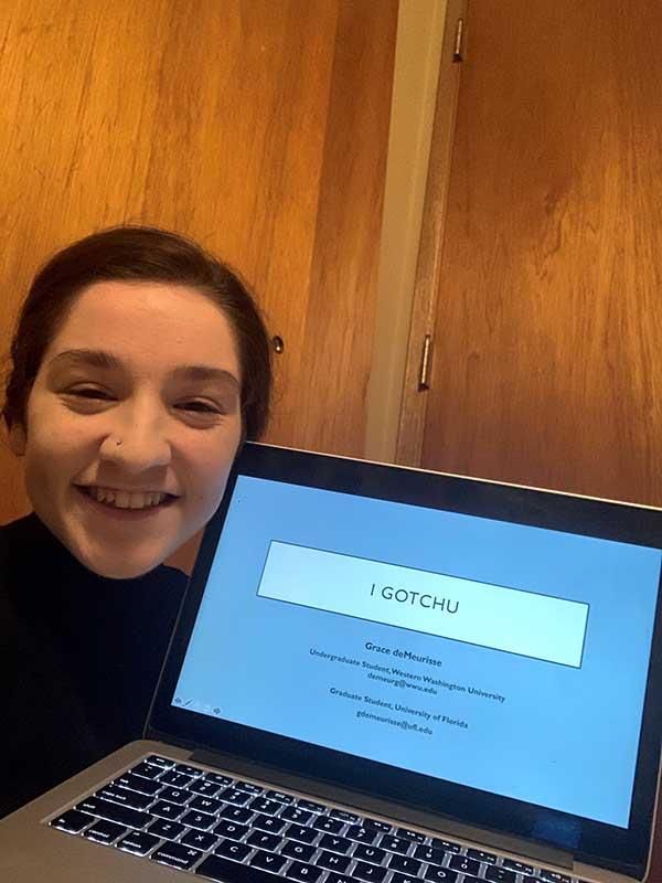 Grace deMeurisse poses next to a screen with "I Gotchu" displayed