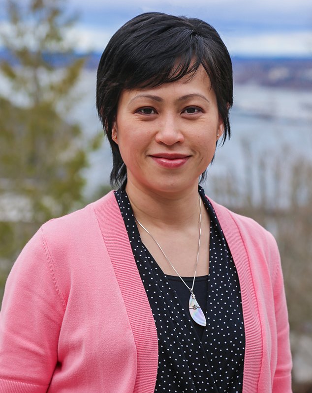 Dr. Ee Lin Lee wears a pink sweater and stands outside in front of Bellingham Bay