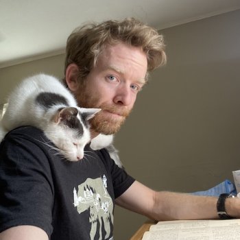 Prof. Tyler Walker with a cat sleeping on his right shoulder