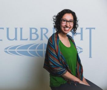 Maria José Palacios Figueroa posing in front of a Fulbright banner in kelly greenshirt and striped shawl